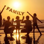 Happy family standing on the beach at the sunset time.
